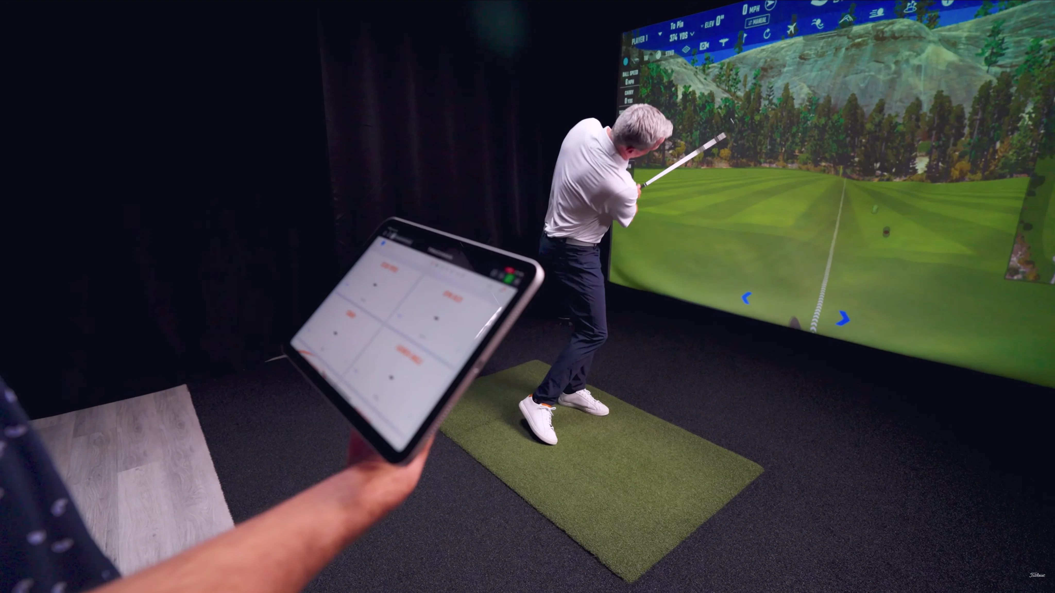 A man swinging a golf club in front of a large screen in a golf simulator bay.
